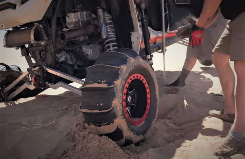 Men digging tire of off-roader out of sand