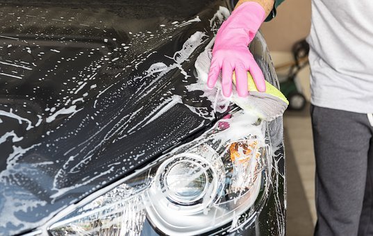 man washing fron of a car with sponge