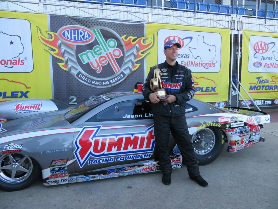 jason line holding a wally trophy near his nhra pro stock camaro