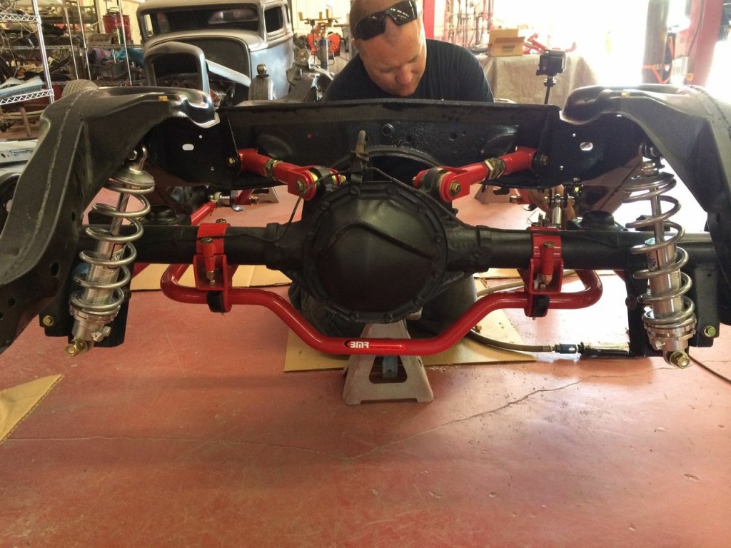 man working on the rear axle and suspension of a hot rod