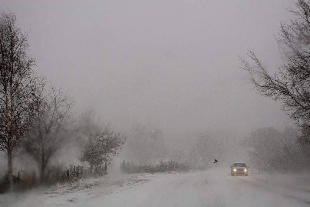 car driving on snow covered road in blizzard