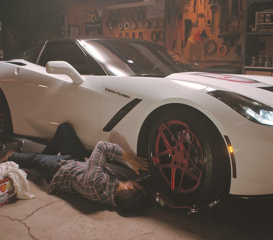 man working underneath c7 corvette in garage at night