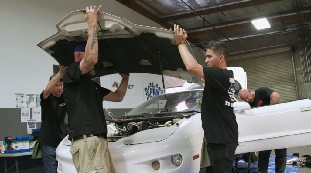 men removing the hood of a fourth-generation pontiac firebird