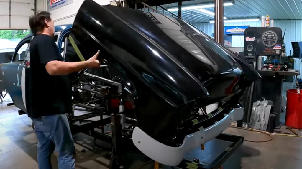 man fitting front tilt hood front clip on a 1955 chevy race car