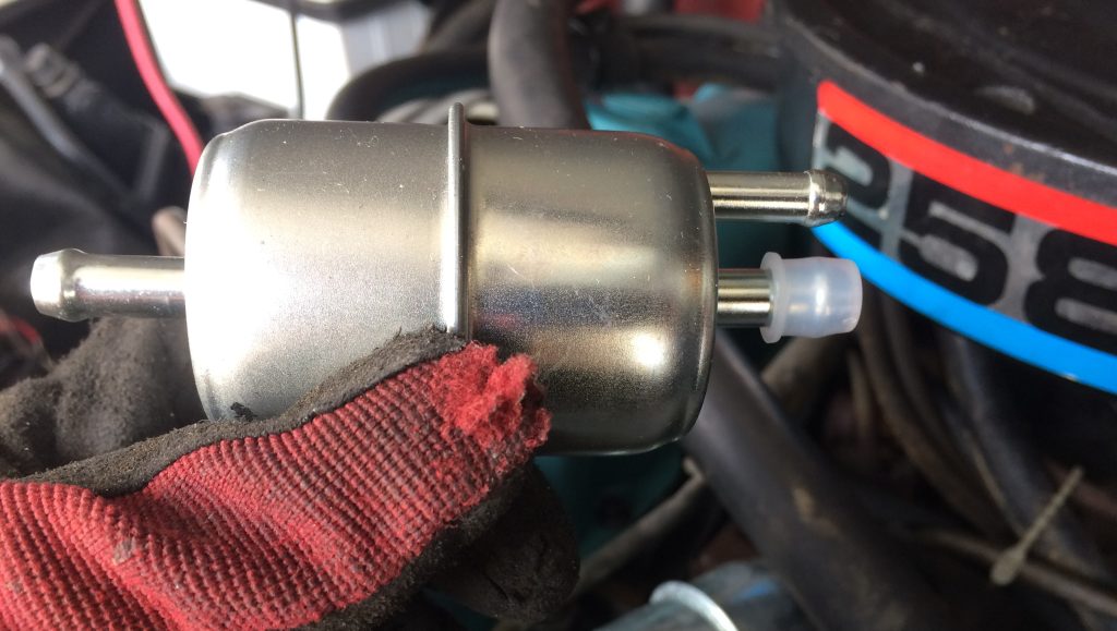 man holding two outlet fuel filter in front of an amc 3258 inline six engine