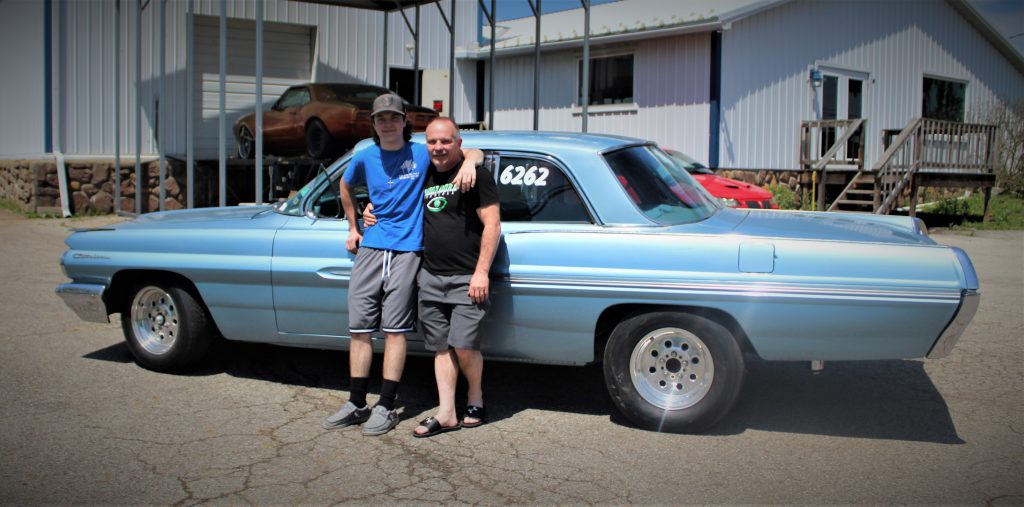 a father and son posing next to their 1962 pontiac catalina drag race car