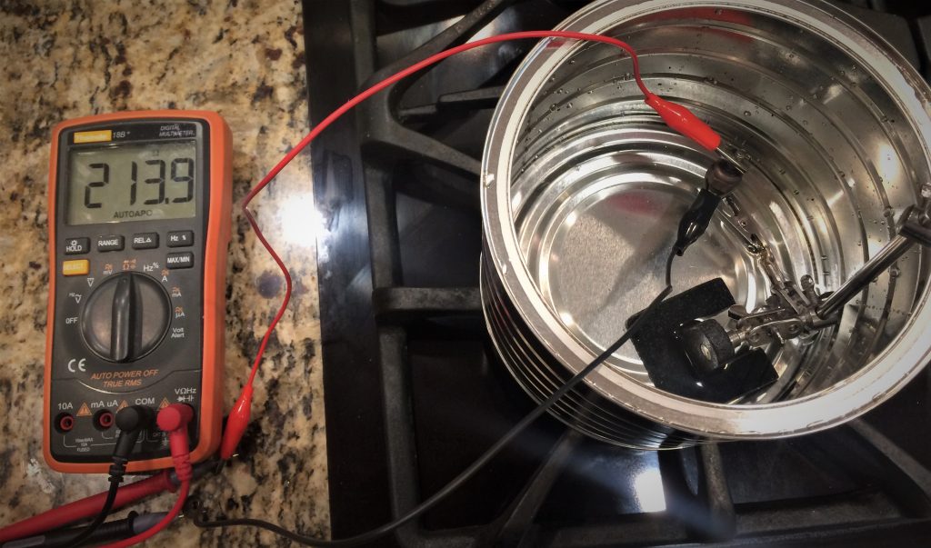 a multimeter next to pot of cool water to test resistance of an electrical temperature gauge sending unit