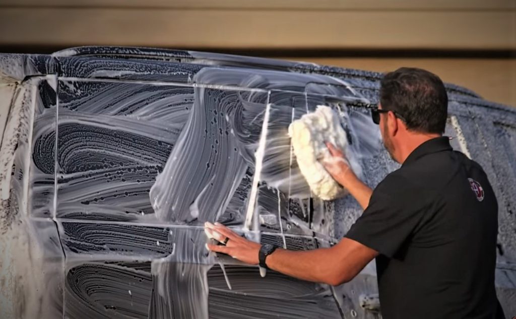 Man Washing full size GM SUV with sudsy water and foam mitt