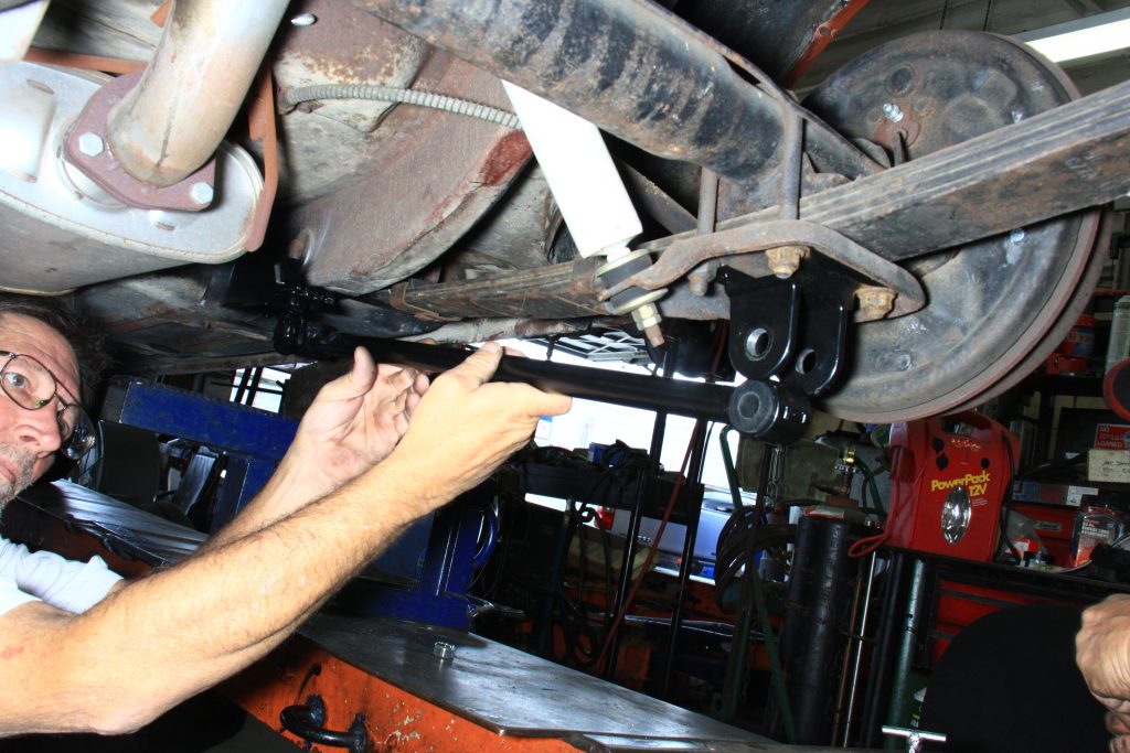 man fitting traction bar to a vintage ford mustang