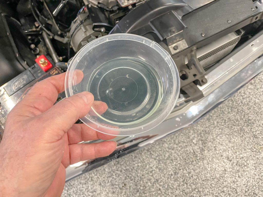 man holding a small pan of water near an engine