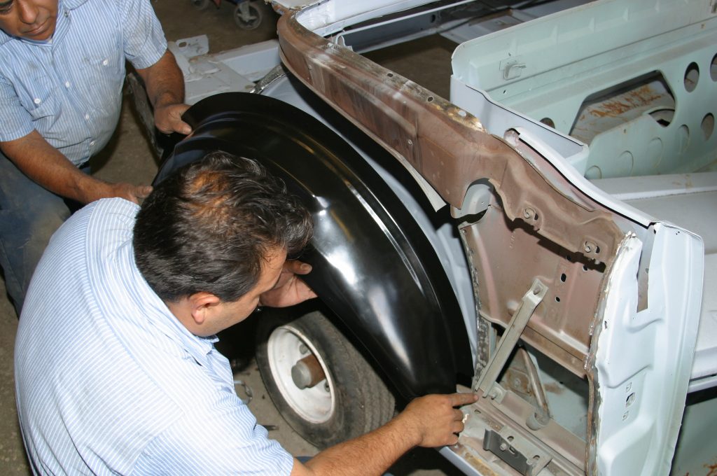 men fitting inner fender into a vintage car body