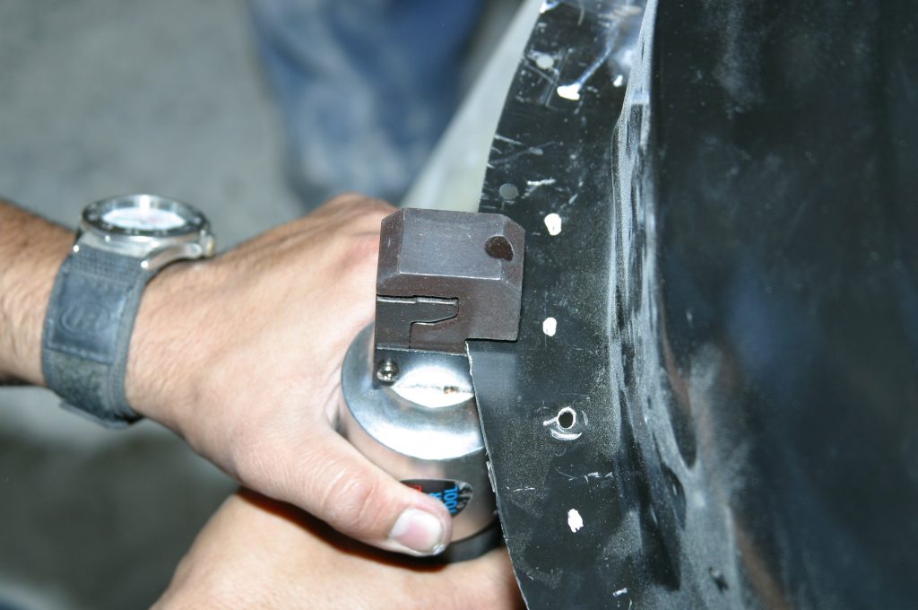 using a metal punch tool on a car fender