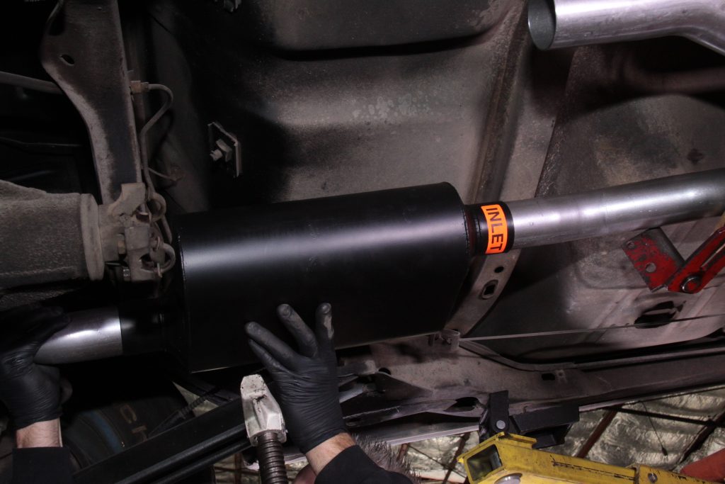 man fitting a muffler into a classic car