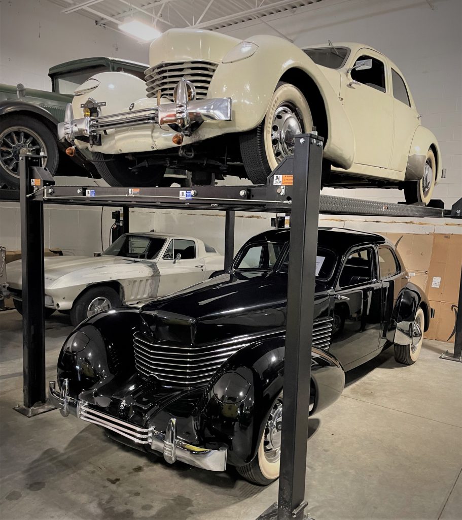 a pair of prewar cord coupes stack atop a lift