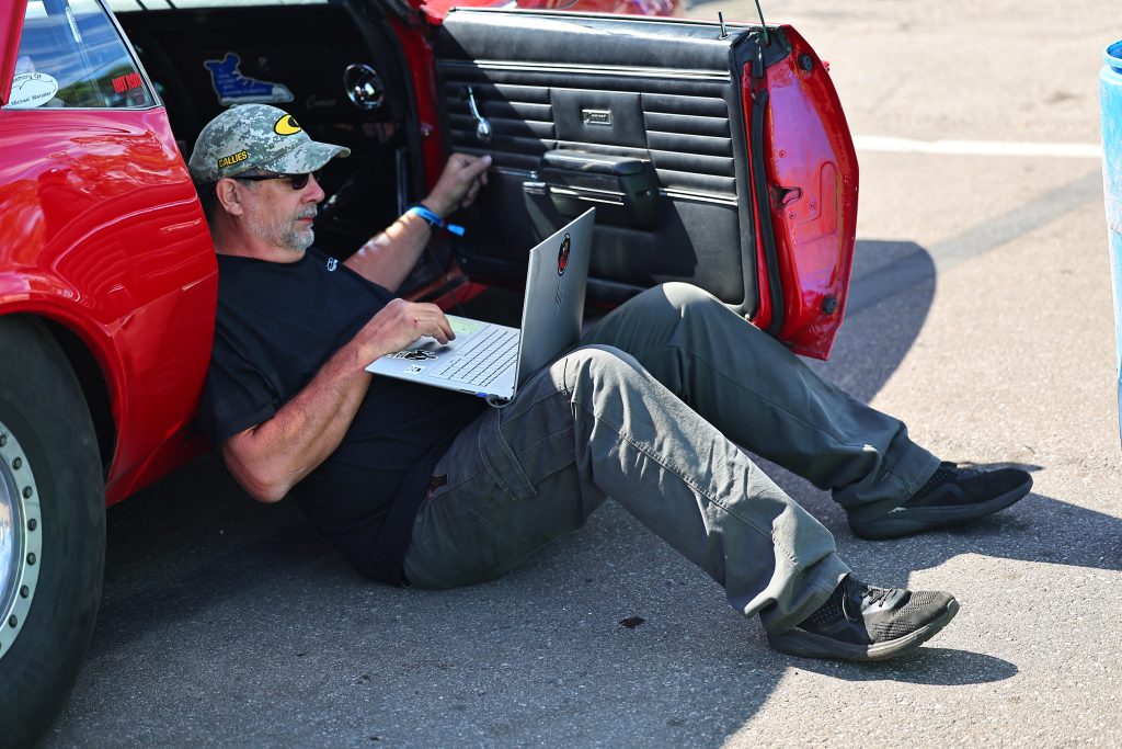 man resting in doorframe of car with laptop
