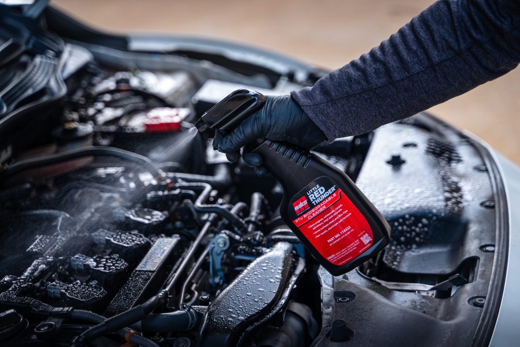 man spraying degreaser onto a car engine
