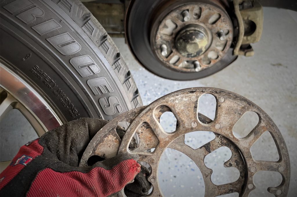 hand holding two wheel spacers near rear wheel of a car