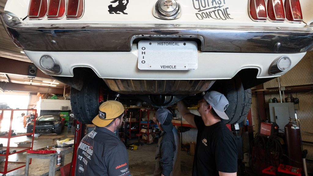 Men working underneath a vintage Mustang on a lift